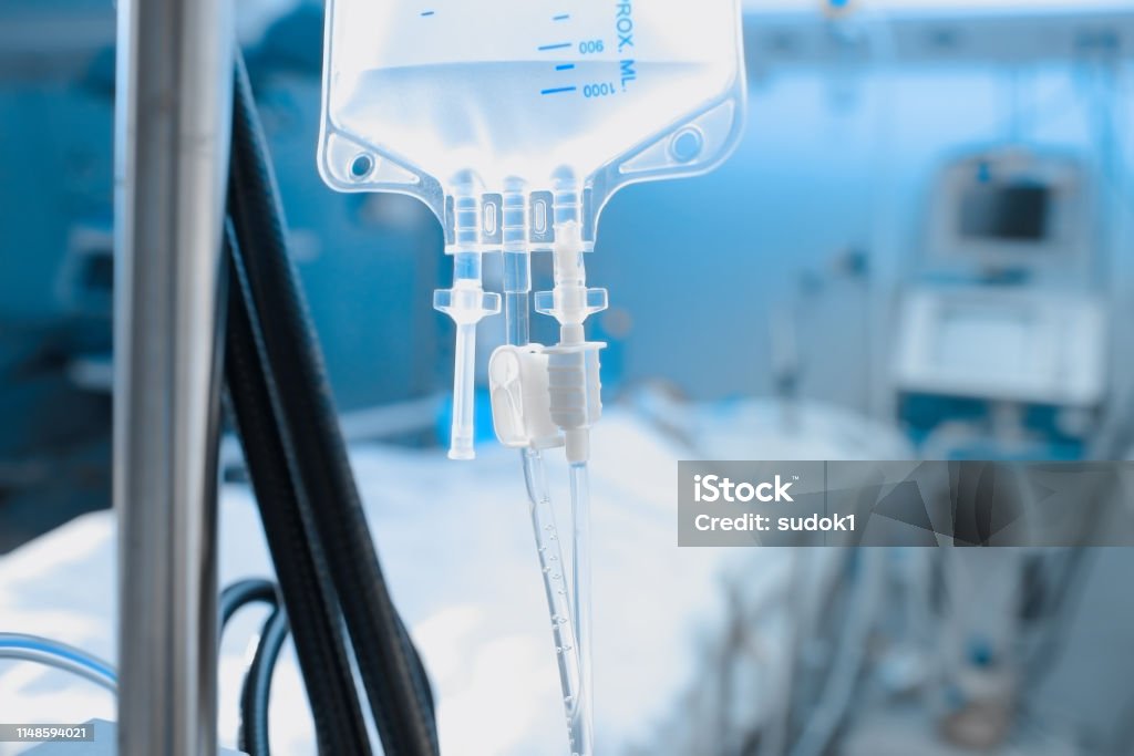 Intravenous drip on the background of patient under the heart monitoring Intravenous drip on the background of patient under the heart monitoring. Intensive Care Unit Stock Photo