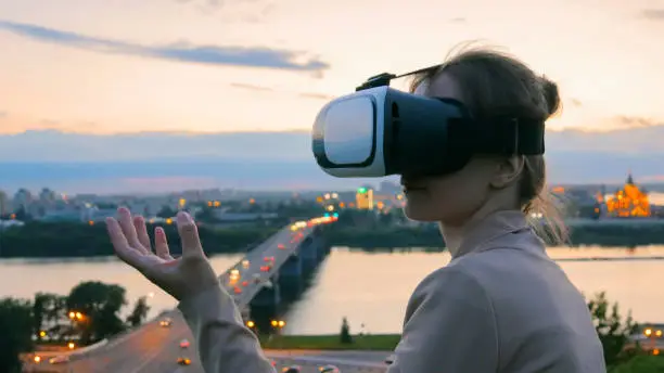 Photo of Woman uses virtual reality glasses in the city after sunset