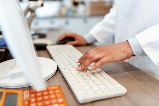 Closeup of pharmacist's hands typing on a computer keyboard at the pharmacy counter. Photo of a female pharmacist using a computer at the hospital pharmacy. Pharmacist searching for a product in the computer database, healthcare, and technology concept.