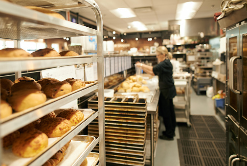Shot of a rack of freshly baked goods with a woman working in the background at a bakery