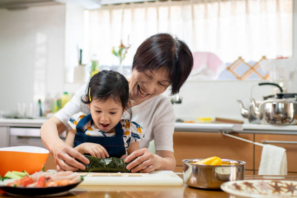 großmutter und enkelin machen gemeinsam sushi - sushi japanese culture food domestic kitchen stock-fotos und bilder