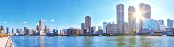 istock Wide angle vibrant panoramic view of sunset  Sumida river under blue sky in Tokyo with sunbeams, wavy water, boats, bridge and skyscrapers 1148604208