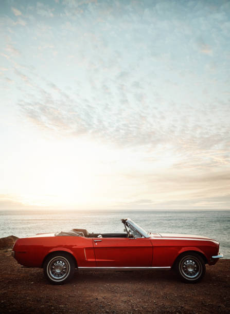 Summer invites you to take a road trip Shot of an empty vintage car parked along the coast at sunset convertible photos stock pictures, royalty-free photos & images