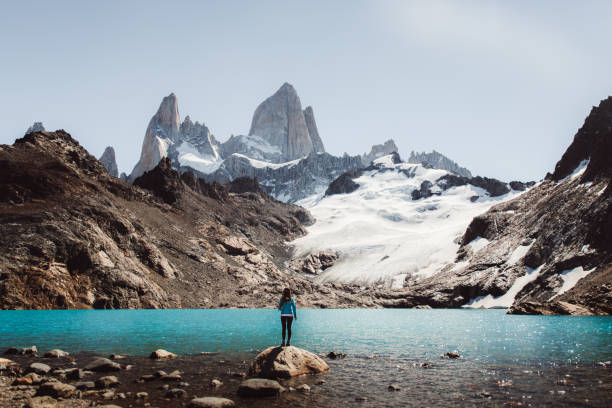 Woman looking at Fitz Roy mountain and turquoise lagoon in El Chalten, Argentina Young woman enjoying a day at Argentinian Patagonia - hiking to Fitz Roy mountain and lagoon De Los Tres during bright warm summer day mt fitzroy photos stock pictures, royalty-free photos & images