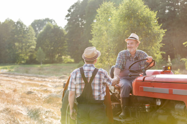istock Farmer shaking hands with coworker sitting on tractor at farm 1148611281