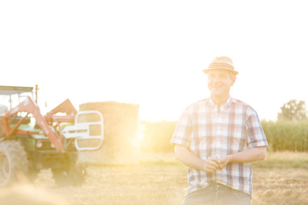 istock Smiling mature farmer standing against harvester at farm 1148611628