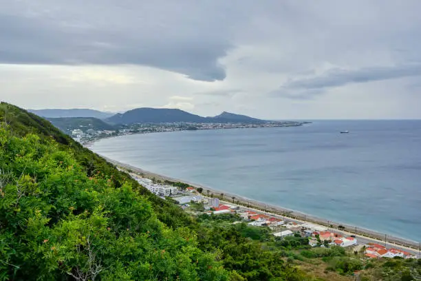 View of Rhodes with the coast leading through the whole picture and heavy clouds in the sky and green plants in the foreground