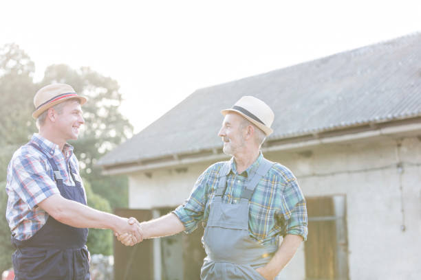 istock Farmers shaking hands while standing against barn at farm 1148615828
