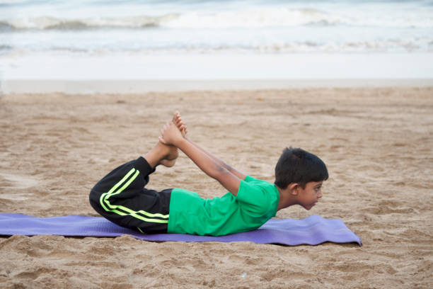 Boy practicing yoga bow pose on the beach Boy practicing yoga dhanurasana pose at beach indian boy barefoot stock pictures, royalty-free photos & images