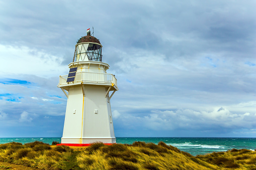 The famous snow-white lighthouse of Waipapa is visible on the horizon. Scenic South Island on a cloudy windy day. Independent trip to New Zealand. The concept of ecological, active and photo tourism