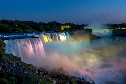 Niagara falls in the summer during beautiful evening, night with clear dark sunset blue sky. Niagara fall water hit with many colorful lights that is beautiful in a way. Sky turning dark and cold.