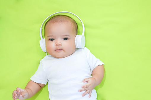 Newborn Asian baby wear white headphone on light green background