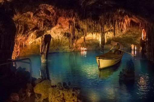 Palma de Mallorca, Spain - May 21, 2018: Emerald lake and old boat among natural rock formations inside Cuevas del Drach in Mallorca island