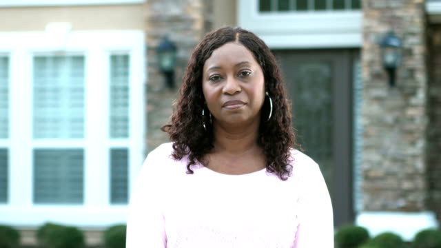 Mature African-American woman standing in front of house