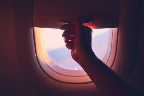 Travel by airplane. Hand pulling down or up window blinds during flight.