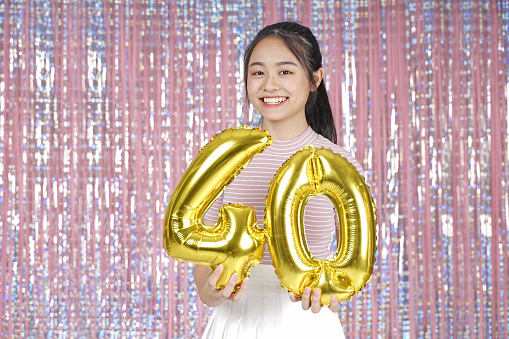 Asian young teenager pretty cheerful beautiful girl with party gold foil balloon, on pink sparkling background