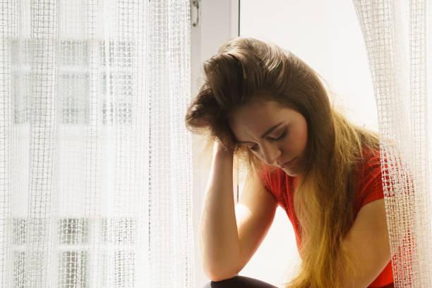 istock Sad woman sitting on windowsill 1148646920