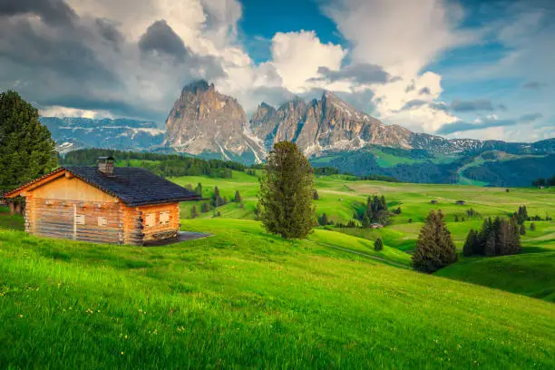 Photo of Green fields with wooden house and high mountains at sunset