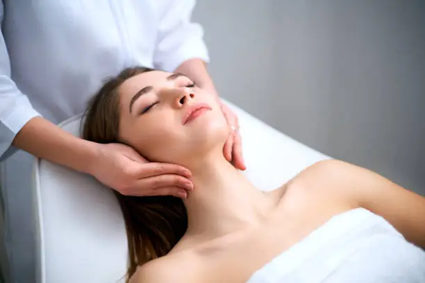 Beautician cleaning woman's face. Spa skincare treatment. Cosmetologist with patient on medical chair at exam room. Healthy skin cosmetology. Masseur making relax facial massage procedure. Doctor touching neck.
