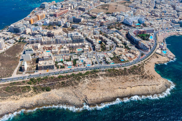 Seaside cliffs, colourful houses and streets of Qawra town in St. Paul's Bay area in the Northern Region, Malta. Popular tourist resort between Bugibba and Salina. Aerial view. Malta island from above stock photo