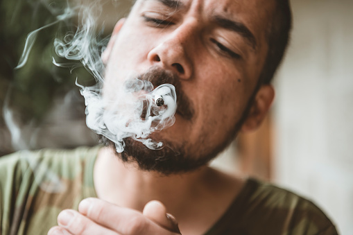 A man smokes cannabis weed, a joint and a lighter in his hands. Concepts of medical marijuana use and legalization of the cannabis.