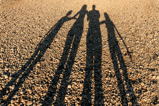 Long shadows of four member family on the beach at sunset. Parent with daughter and son silhouette