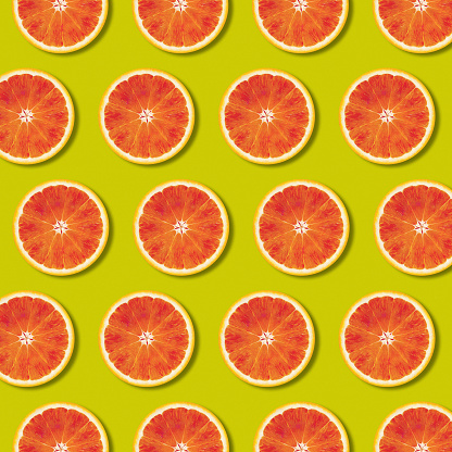 Geometric red orange fruit slices pattern on green color background. Minimal flat lay, top view food texture