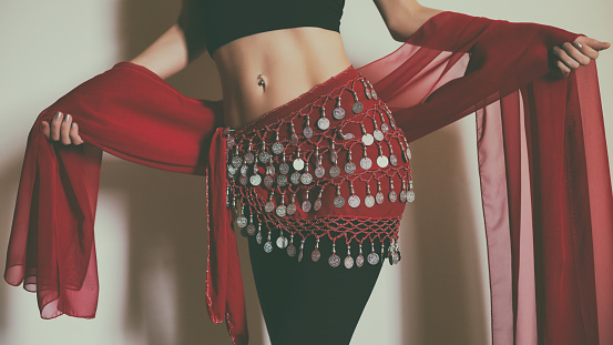 Image of close up stomach of belly dancer holding red scarf .Toned photo.