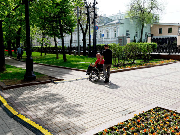 Moscow, Russia - May 10, 2019: a wheelchair user and a man helping him for a walk in Chistoprudny boulevard