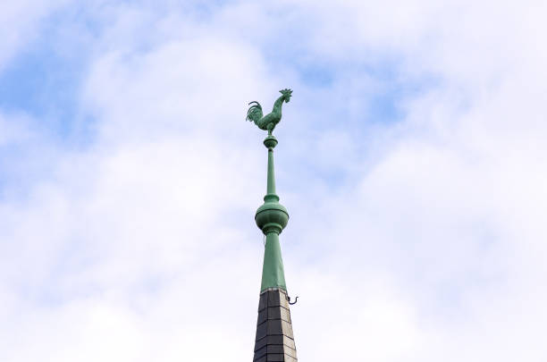 Close up of a old historic tall tiled spire on a roof surmounted by the figure of a cock