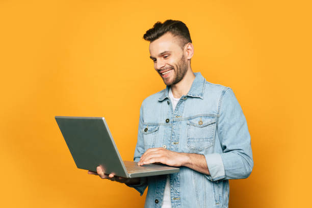istock Modern young student or business man is working with laptop in hands on yellow background 1148667072