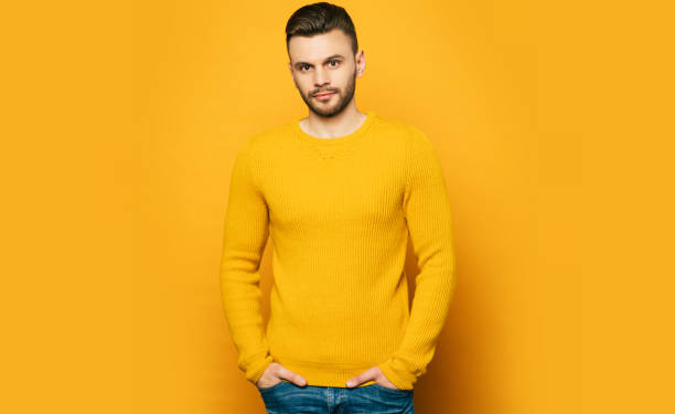 istock Confident handsome man in yellow is posing over orange background and looks on camera 1148667097