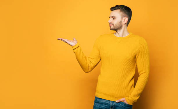 istock Handsome man shows something on his palm on copy space while standing over yellow background 1148667100