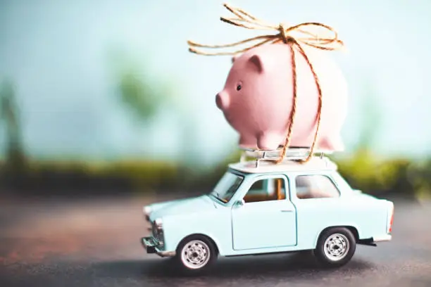 Photo of Little pink piggy bank tied to the top of an old car