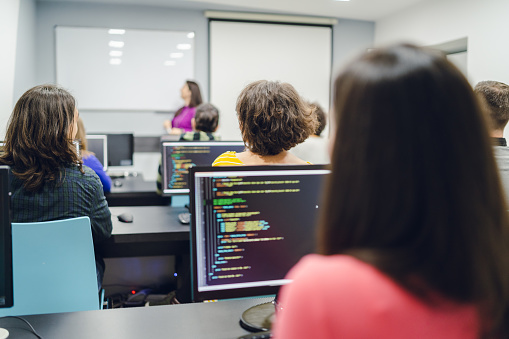 Female professor teaching programming to group of young people in computer lab