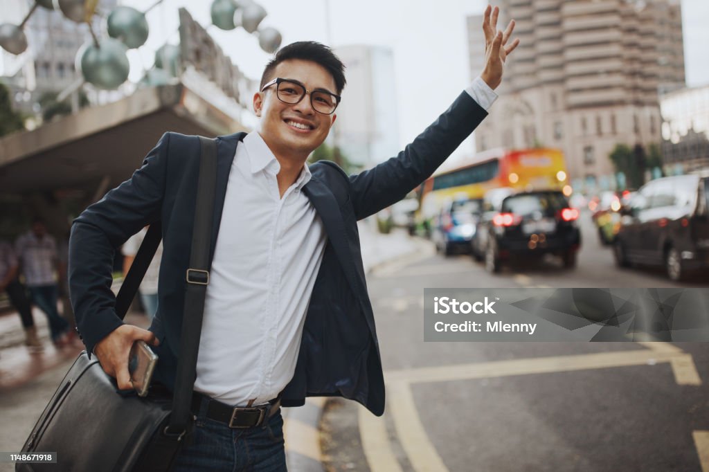 Businessman Hailing Taxi Kuala Lumpur Young malaysian businessman at a bus and taxi stand in the streets of downtown Kuala Lumpur hailing for a taxi with a smile. Kuala Lumpur, Malaysia, Asia Hailing A Ride Stock Photo