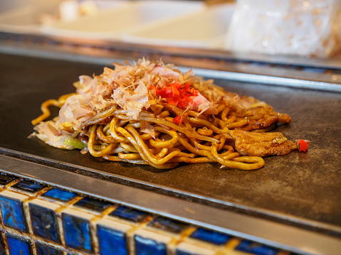 Closeup detail of a freshly cooked Yakisoba topped with Katsuobushi fish flakes, sauce, and ginger, on a Teppan grill. Shallow focus. Dotonbori, Osaka, Japan. Travel and cuisine.