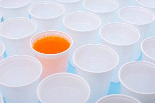 istock Disposable plastic white empty cups and one glass filled with orange lemonade 1148681410