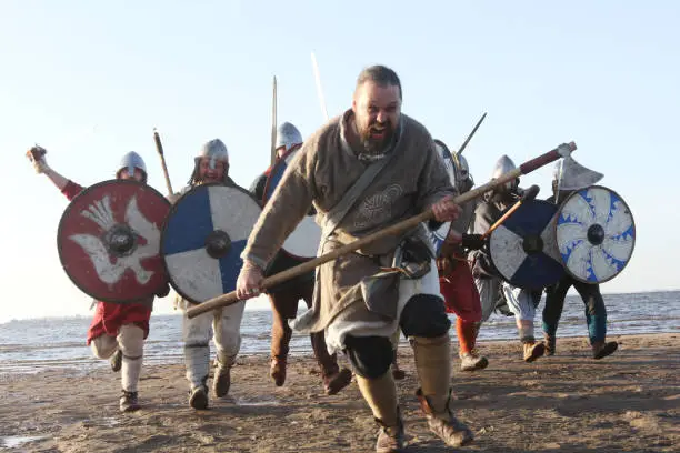Slavic warriors reenactors with wearpons and shields training fighting outdoors at seaside , running at camera