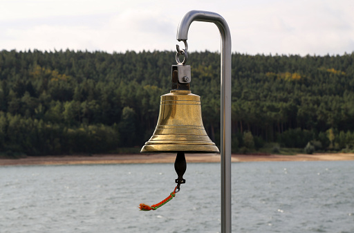 Copper bell on a yacht on the background of the coastline.