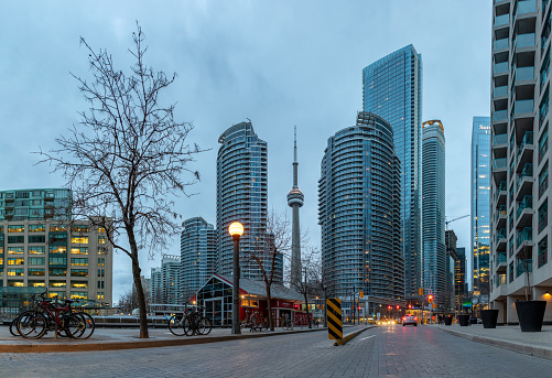 A panorama picture of the CN Tower peeking through nearby buildings in downtown Toronto.