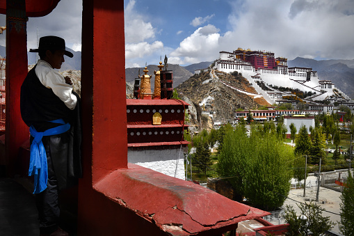 Tibetan man in traditional dress, overlooks The Potala Palace (one time residence of the Dalai Lama) from a nearby monastery in Lhasa, the capital city of Tibet.