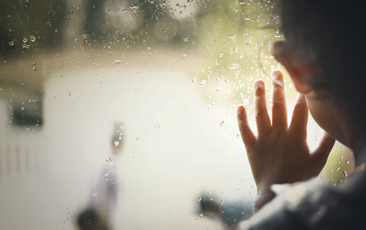 Little girl  by window with raindrops on it on a rainy day.Background.