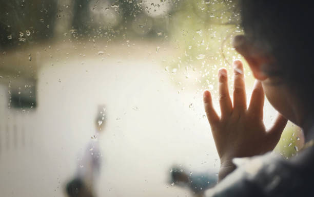 Little girl  by window with raindrops on it on a rainy day stock photo