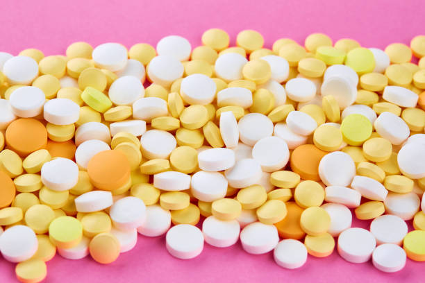 montão dos comprimidos amarelos e alaranjados brancos no fundo cor-de-rosa - painkiller vitamin pill full frame macro - fotografias e filmes do acervo