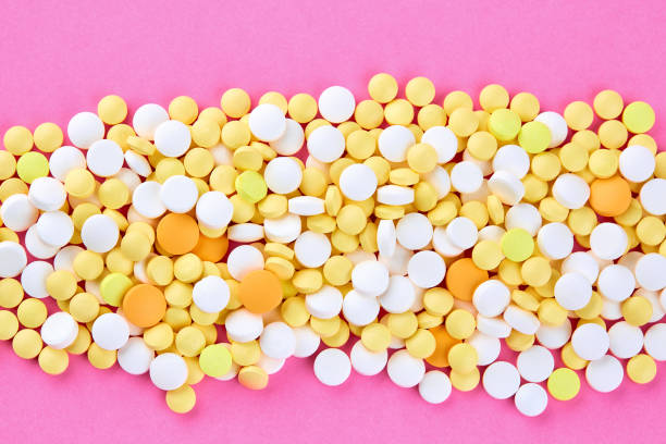 montão dos comprimidos amarelos e alaranjados brancos no fundo cor-de-rosa - painkiller vitamin pill full frame macro - fotografias e filmes do acervo