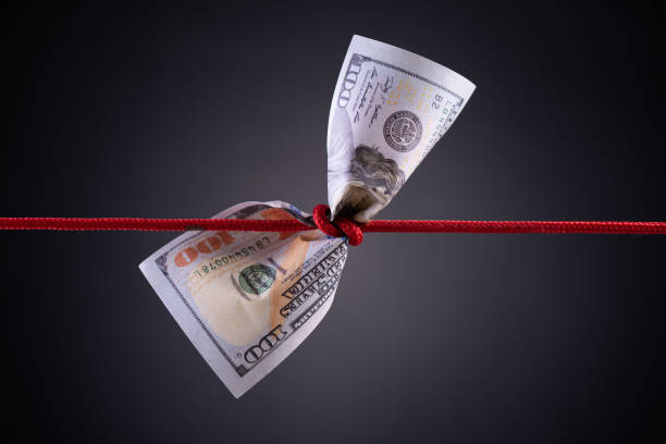 American dollar tied up in red rope knot on dark background with copy space. business finances, savings and bankruptcy concept. American dollar tied up in red rope knot on dark background with copy space. business finances, savings and bankruptcy concept. inflation economics stock pictures, royalty-free photos & images
