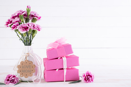 Happy mothers day concept. Gift box with pink carnation flower on white wooden table background.
