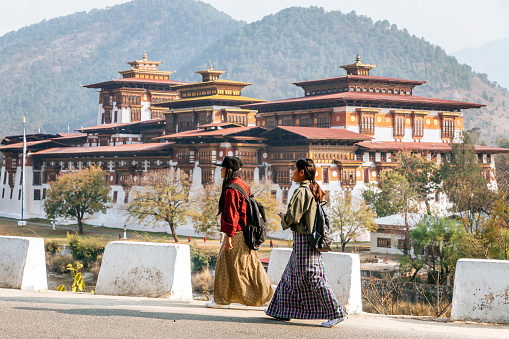 Two women are walking on a road in front of Punakha Dzong which is arguably the most beautiful dzong in the country,