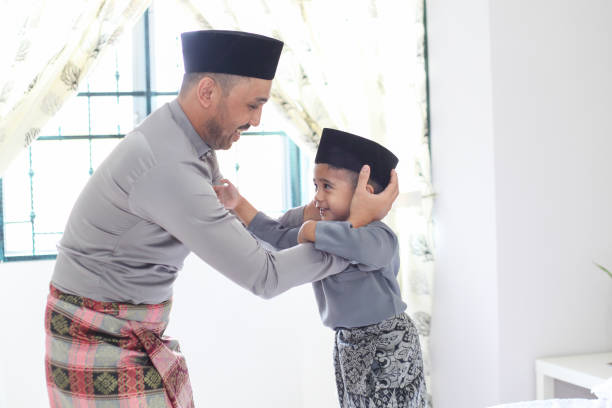 A Father Helping His Son To Wear a Songkok A father helping his son wearing a songkok on Hari Raya Aidilfitri / Eid-Ul-Fitr in Malaysia. hari raya family stock pictures, royalty-free photos & images